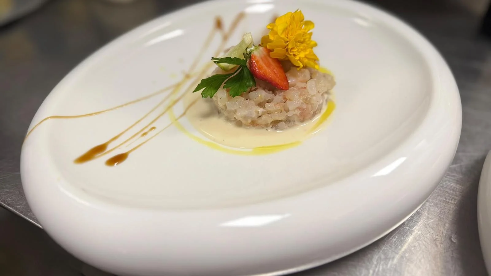 Una tartare impiattata con fragola e un fiore giallo
